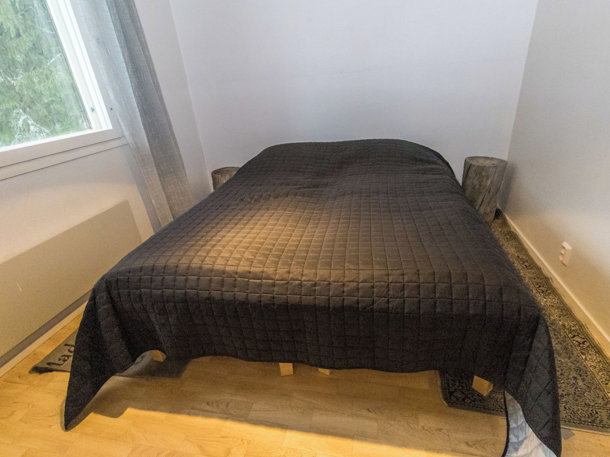A bed with a quilted cover in a room with a window and a wooden floor.