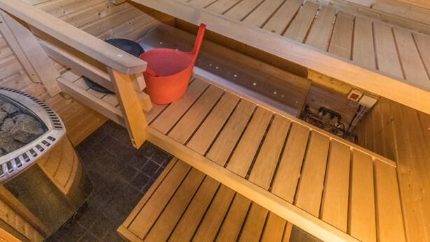 Eine Sauna mit Holzbänken und einem roten Eimer.