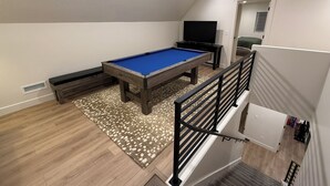 Une table de billard dans une pièce dotée d’un plafond en pente, d’un téléviseur et d’un escalier.
