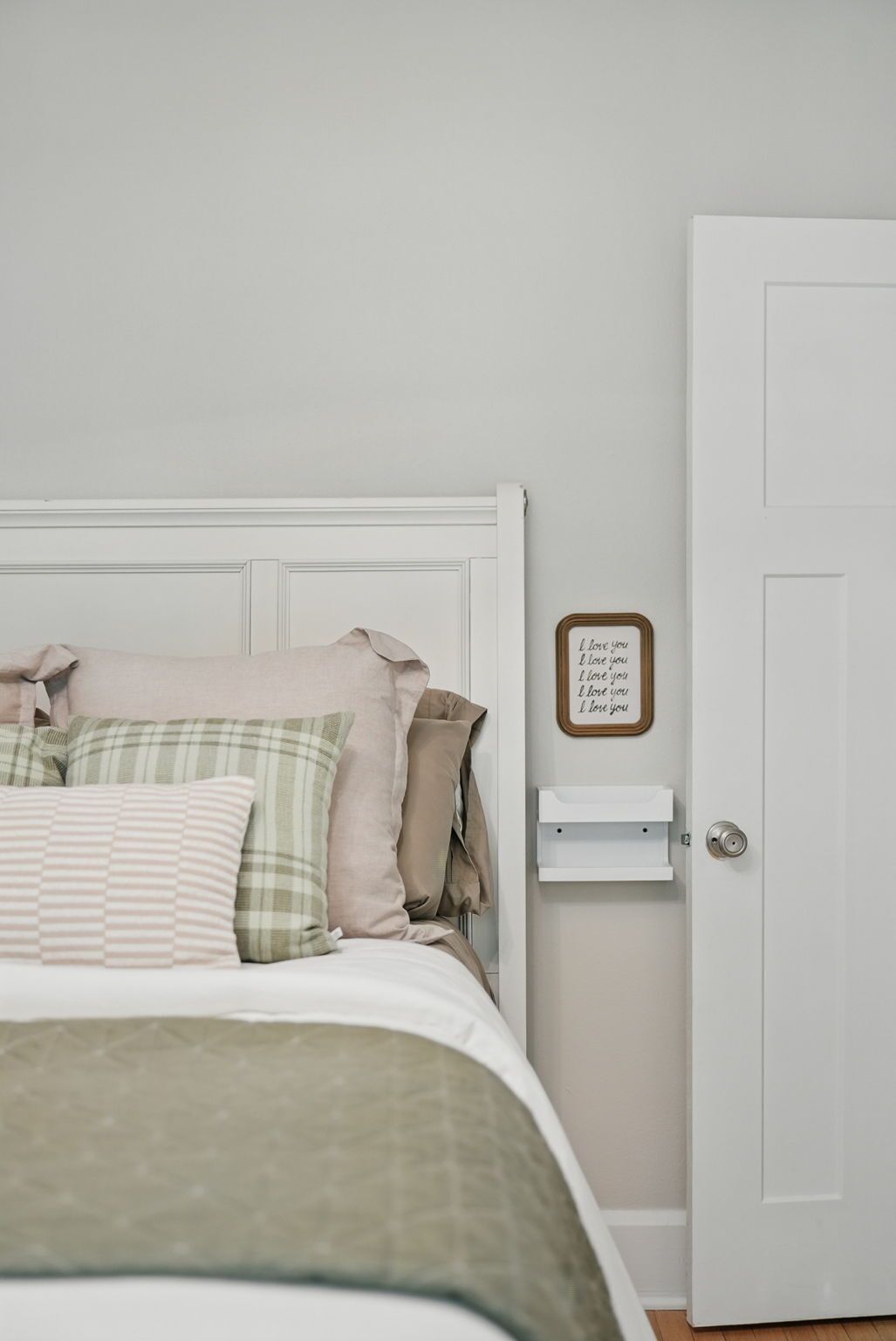 Een slaapkamer met een bed, kussens, een nachtkastje en een deur.