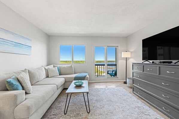A modern living room with a sofa, a coffee table, a TV, and a view of a balcony.
