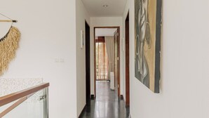 A hallway with a glass railing, a painting on the wall, and a door at the end.