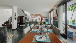 A spacious dining area with a long table set for a meal, a staircase leading to another level, and a view of a pool through large windows.