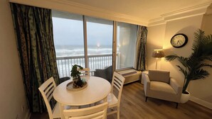Ein Zimmer mit einem runden Tisch, zwei Stühlen, einer Couch, einer Topfpflanze und Meerblick durch große Fenster.