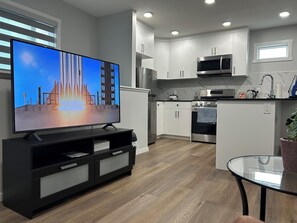 Eine moderne Küche mit weißen Schränken, einer Edelstahl-Mikrowelle, einem Backofen und einem Fernseher auf einem schwarzen Standfuß.