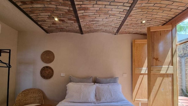 Ein Schlafzimmer mit Ziegeldecke, einem Bett mit weißen Leinen, einem Korbstuhl und einem kleinen Tisch.