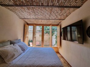 A bedroom with a brick ceiling, a large bed, a TV on the wall, and a view of the outdoors through a window. - Casa Valparaíso (Saltillo)