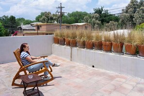 A person seated on a rocking chair on a tiled patio with terracotta pots of dried plants in the background.