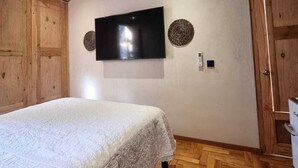 Ein Schlafzimmer mit Ziegeldecke, einem Bett mit weißer Bettdecke, einem an der Wand befestigten Fernseher und einem Holzschrank.