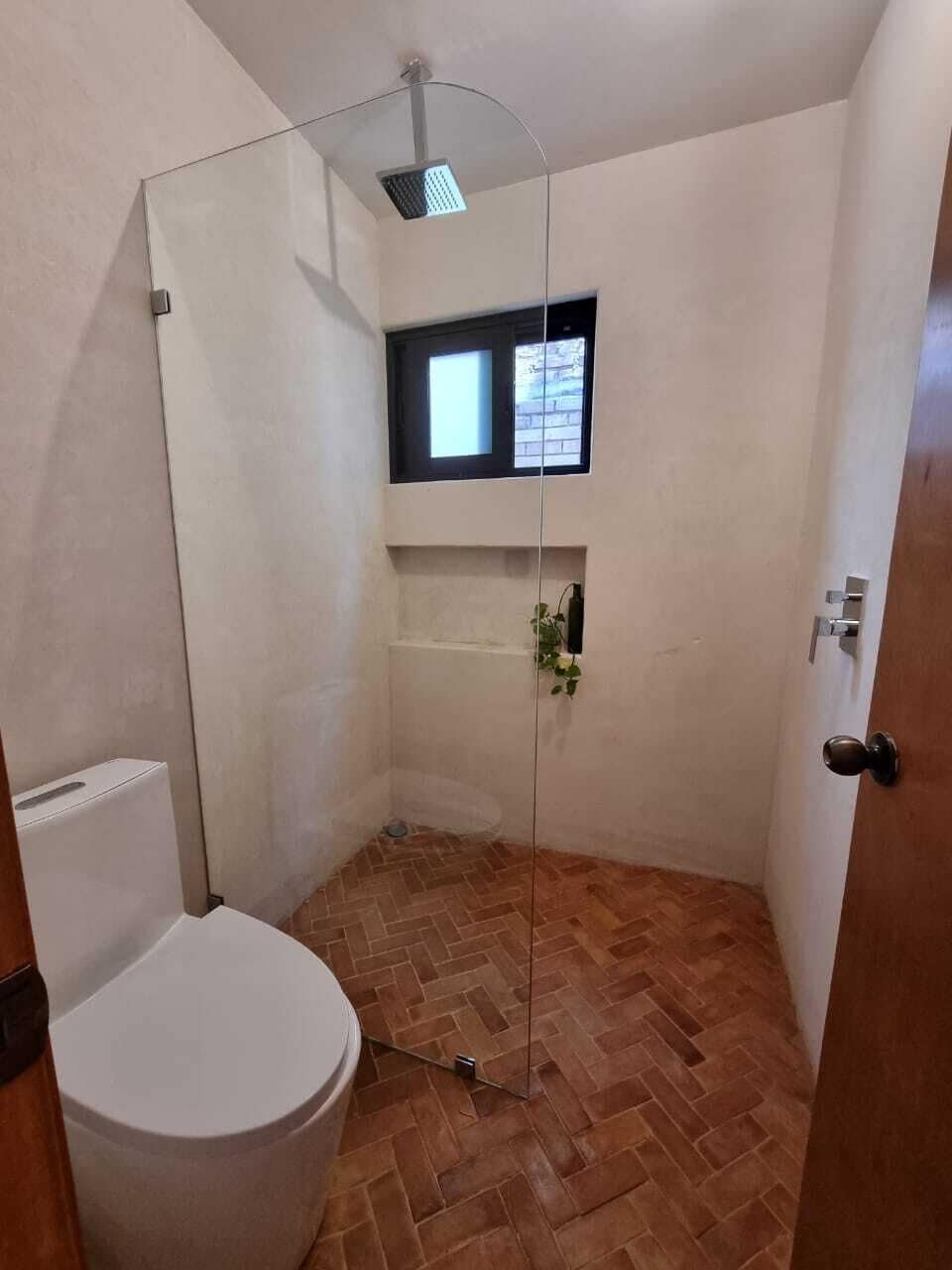 Un baño con ducha, inodoro y una pequeña ventana.