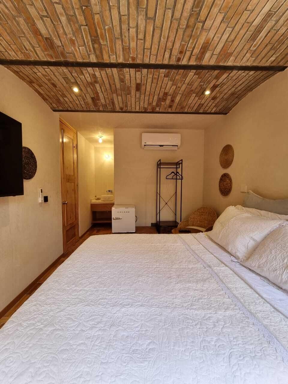 Un dormitorio con techo de ladrillo, una cama, una mesita de noche, un armario y un baño con lavabo y espejo.