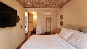 Ein Schlafzimmer mit einem großen Bett, Holzbalkendecke, Klimaanlage und einem an der Wand befestigten Fernseher.