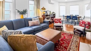 A modern living room with a sofa, ottoman, and a dining area with chairs and a table.