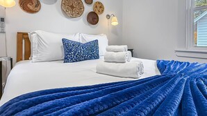 A hotel room with a bed, white bedding, a blue throw blanket, and decorative plates on the wall.