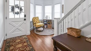 A hallway with a patterned rug, a wooden bench, a yellow chair, and a white door with a window.