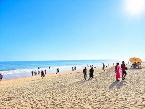 A beach with people walking and standing, a clear sky, and the ocean in the background. - Hotel Aradhya Puri (Puri)