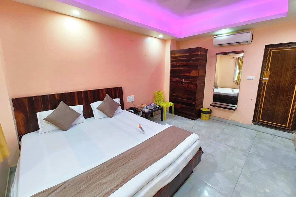Habitación de hotel con cama, armario de madera, una mesita con silla, equipo de aire acondicionado y una puerta.