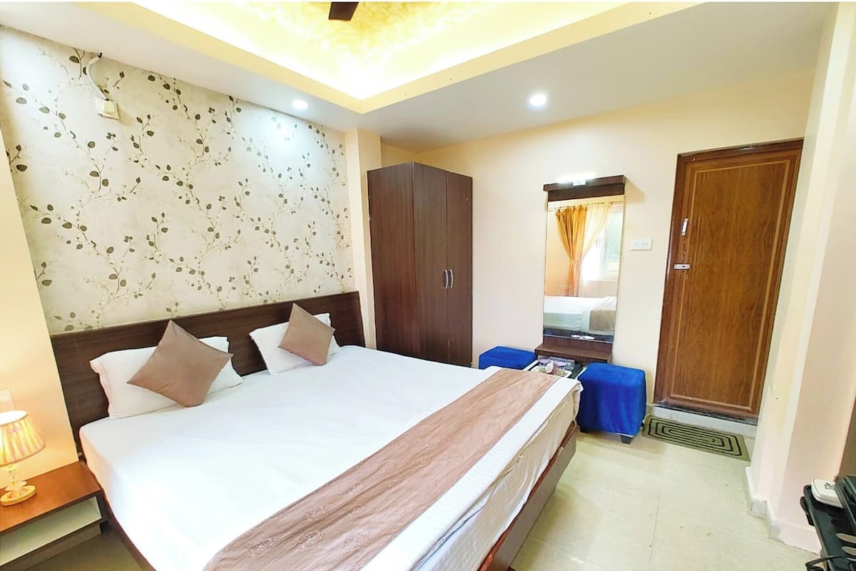 Habitación de hotel con una cama grande, un armario, un espejo y un escritorio con lámpara.