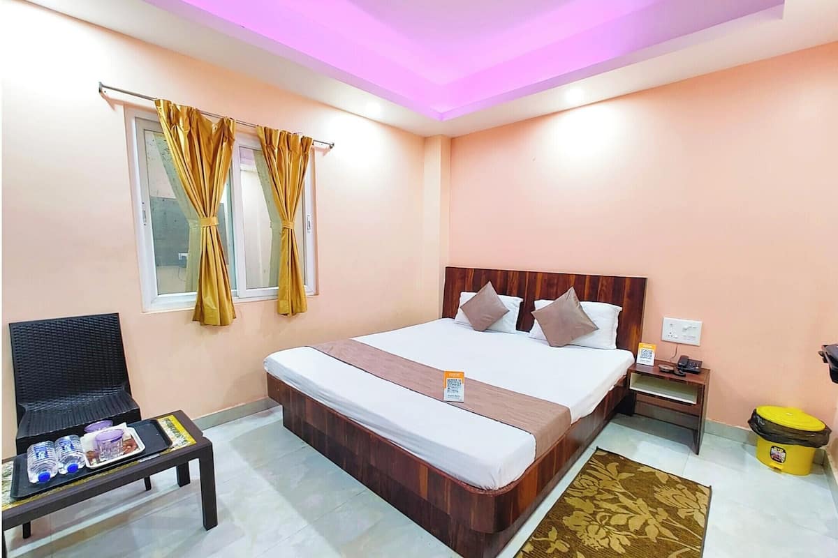 Habitación de hotel con cama, mesita de noche, silla y una pequeña mesa con botellas.