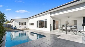 Una casa moderna con piscina, mobiliario de exterior y un patio cubierto.