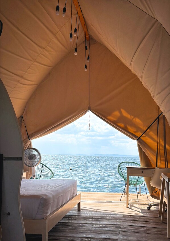 A tent with a bed, a table, and a chair, with a view of the sea.