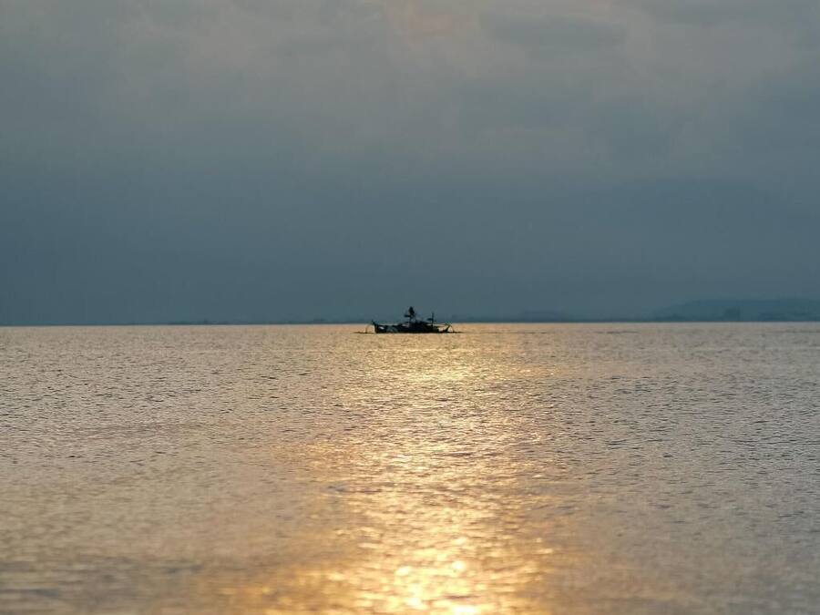 Mar tranquila con un barco a lo lejos y un sol brillante cerca del horizonte.