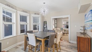 A spacious dining area with a large table and chairs, a chandelier, and a view of the backyard through large windows.