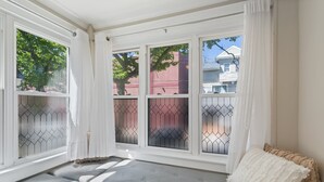 A room with a bench, a window with a view of a tree and a building, and a white curtain.