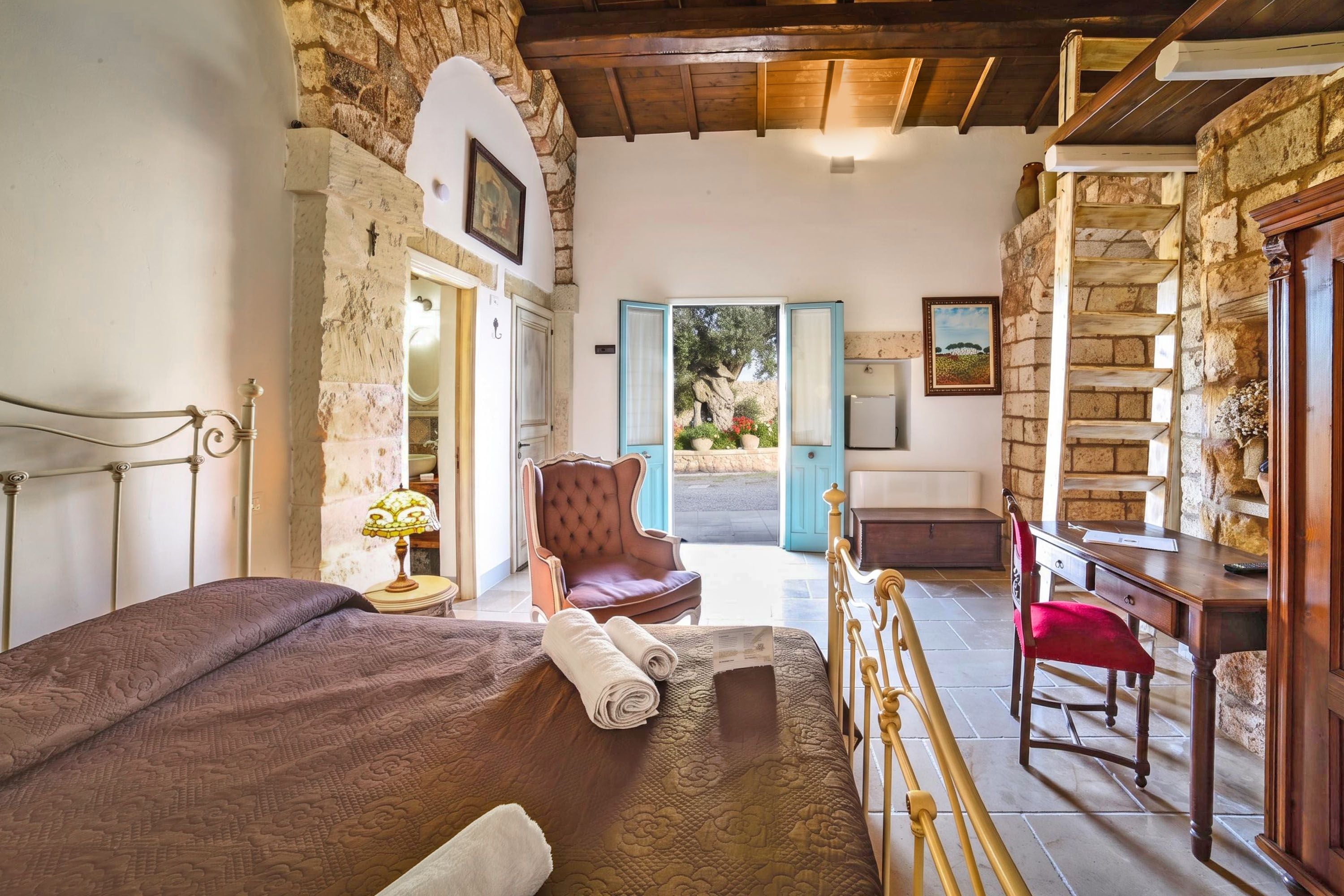 Quarto com cama, cadeira, escrivaninha e vista para o exterior.