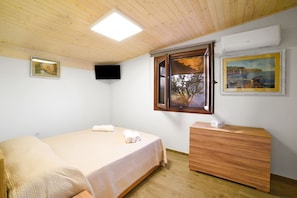 Un dormitorio con cama, cómoda de madera, televisor montado en la pared y ventana con contraventanas abiertas.
