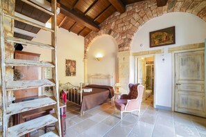 A rustic bedroom with a stone wall, a bed, a chair, and a wooden ladder. - Masseria Santu Lasi With Private Pool & BBQ (Surbo)