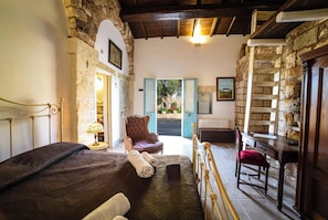 A bedroom with a bed, a chair, a desk, and a staircase.