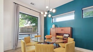A dining area with a glass table surrounded by four chairs, a wooden cabinet, and a window with curtains. - 4BR East Austin Home | Modern & Open Living (Austin)
