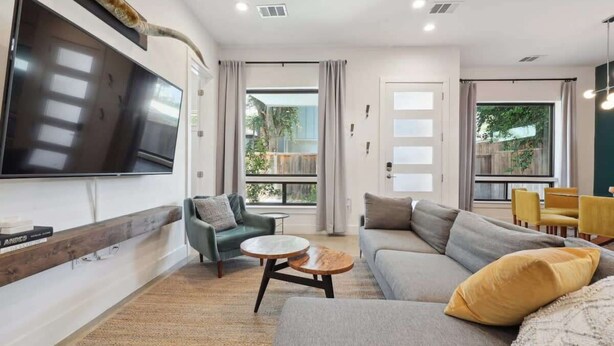 A modern living room with a flat-screen TV, a grey sofa, a green armchair, and a yellow chair. - 4BR East Austin Home | Modern & Open Living (Austin)