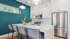 A modern kitchen with white cabinets, a stainless steel refrigerator, a microwave, and a large island with bar stools. - 4BR East Austin Home | Modern & Open Living (Austin)