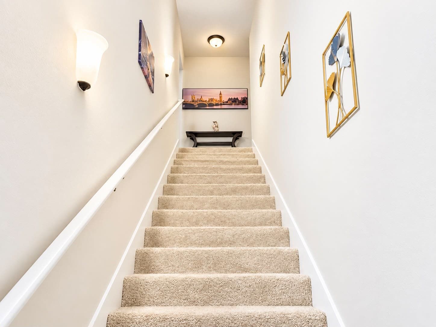 A carpeted staircase with a handrail, a framed picture on the wall, and a light fixture above.