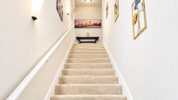 A carpeted staircase with a handrail, a framed picture on the wall, and a light fixture above.