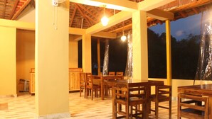 An indoor dining area with wooden tables and chairs, a ceiling fan, and large windows. - Billing View Camp and Mud Houses (Jogindarnagar)