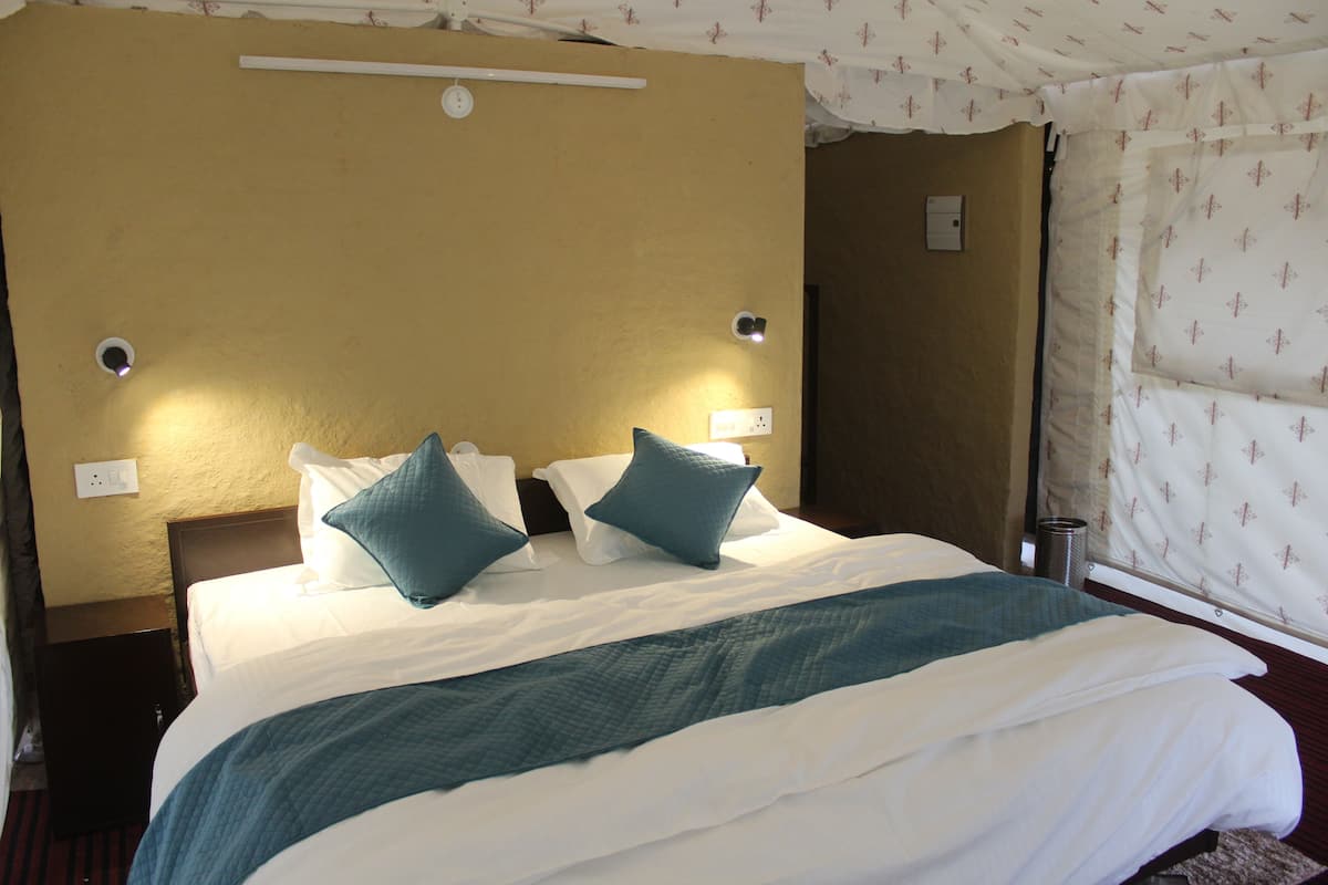 Una camera d'albergo con un letto grande, due luci fissate al muro e una parete spoglia con una presa di corrente.