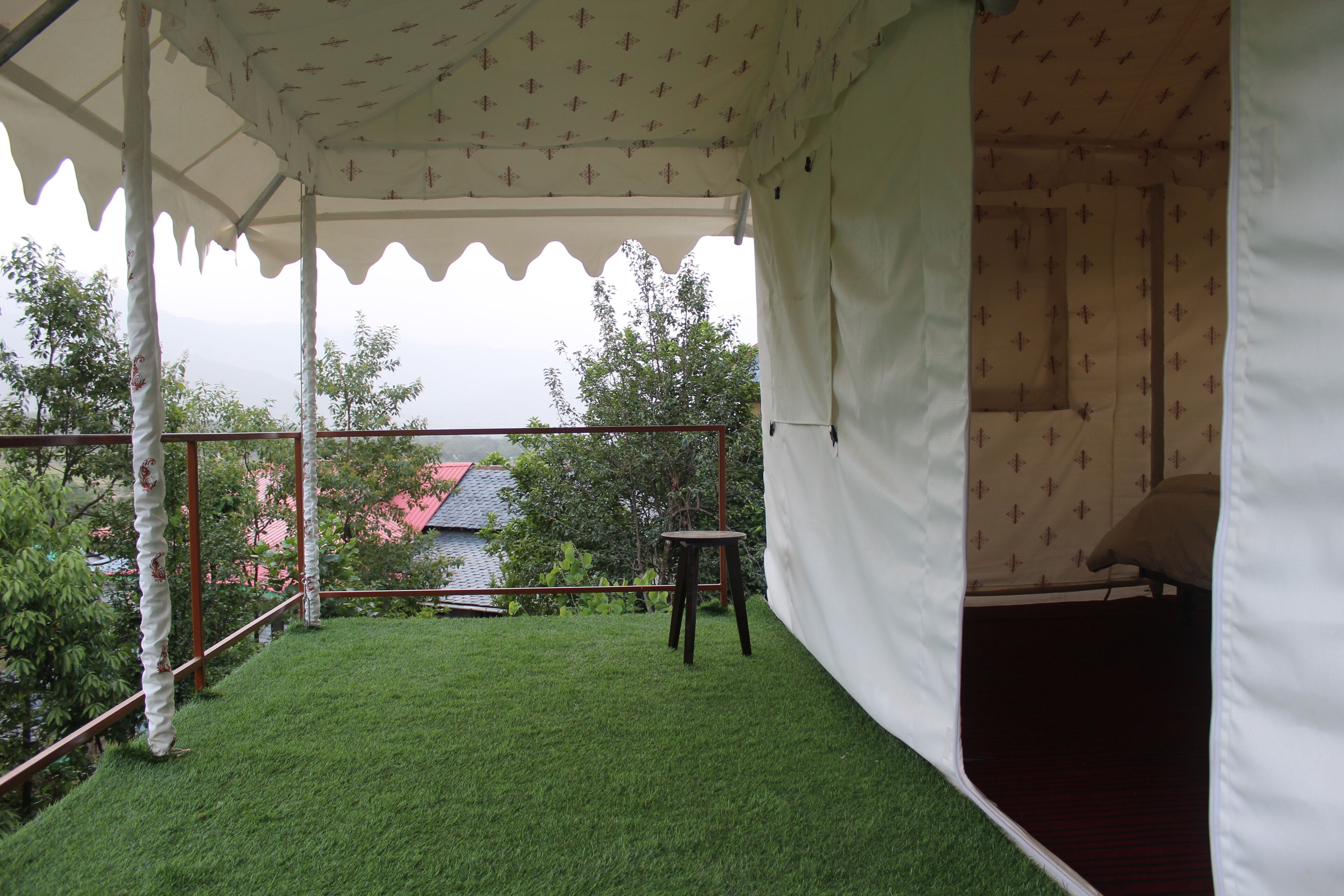 Un espacio al aire libre con carpa, césped artificial, una mesita y una vivienda en el fondo.