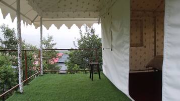 Un espacio al aire libre con carpa, césped artificial, una mesita y una vivienda en el fondo.