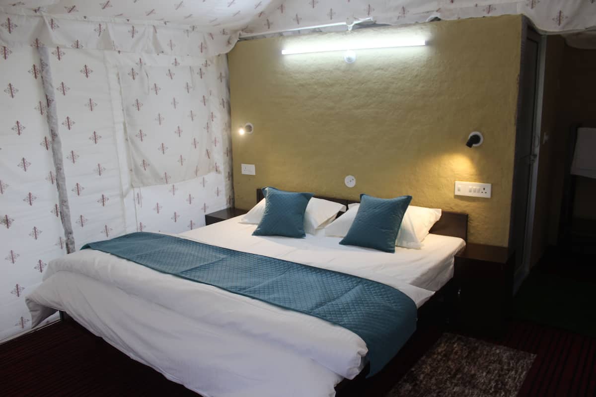 Un letto rifatto con una coperta e cuscini color petrolio, un comodino con una lampada e un punto luce fissato al muro.