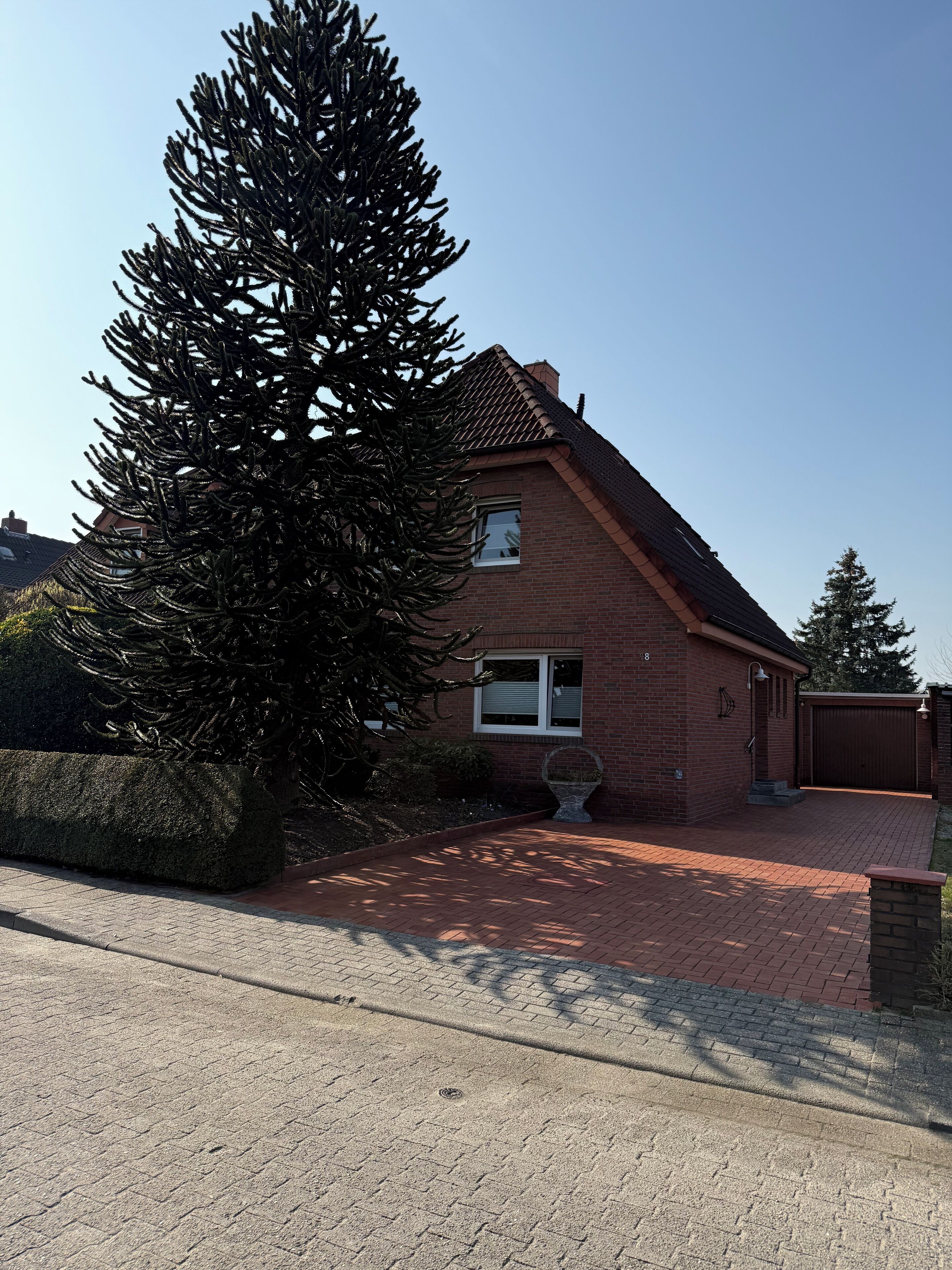 Ein Ziegelhaus mit einem Ziegeldach, ein großer immergrüner Baum im Vordergrund und eine gepflasterte Auffahrt.
