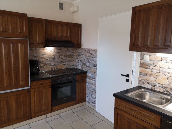 A kitchen with wooden cabinets, a Bosch oven, a black stove, a stone backsplash, and a stainless steel sink. - Quiet vacation apartment very well located in Papenburg (Papenburg)