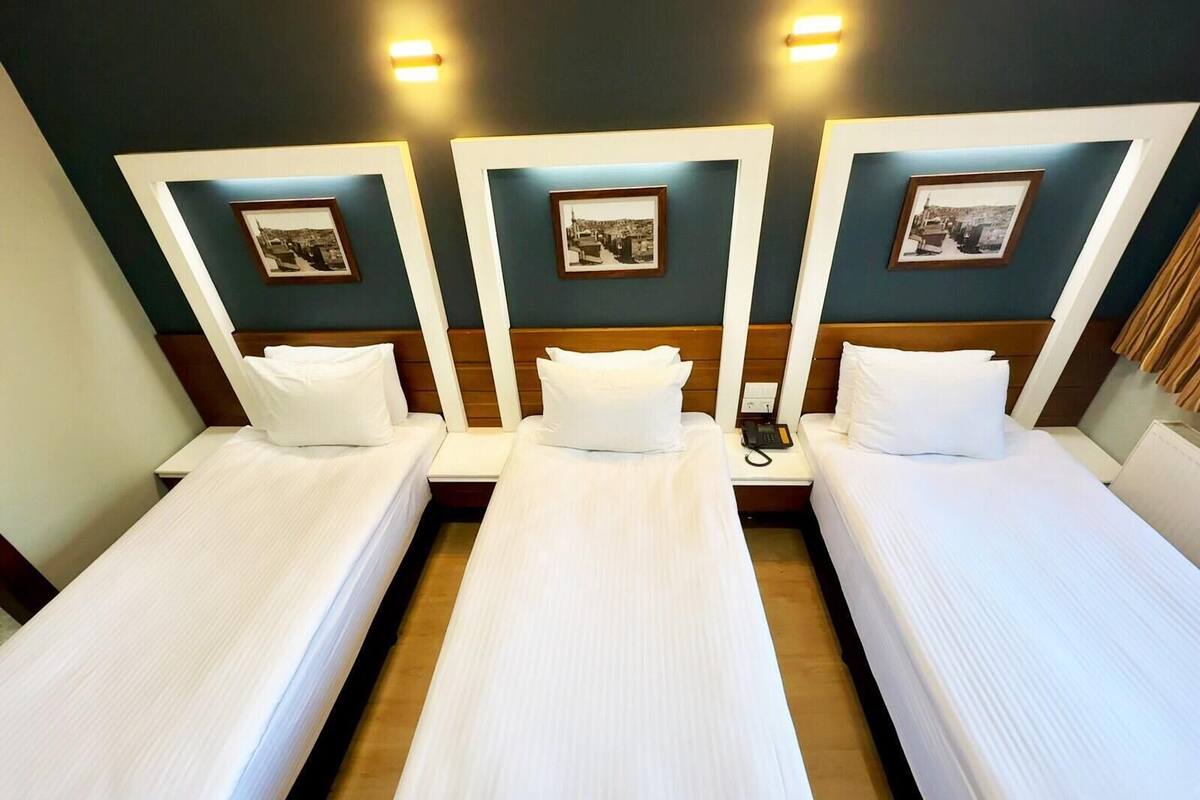A hotel room with three single beds, each with white linens and pillows. There are framed pictures on the wall above each bed.