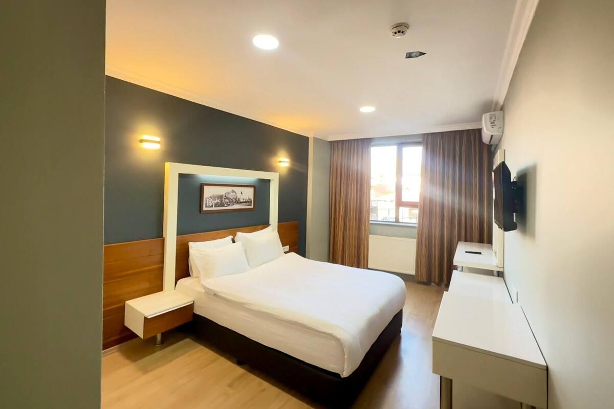 A hotel room with a bed, bedside table, desk, and a mounted TV.