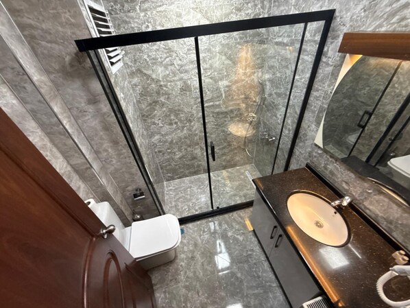 A modern bathroom with a glass shower enclosure, a marble-tiled floor, and a wooden vanity with a sink. - Berlitz Otel (Ankara)