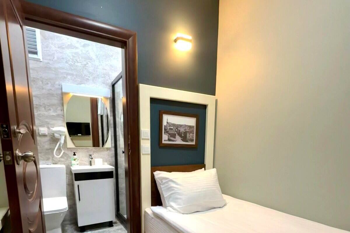 A bedroom with a single bed, a bedside table, a mirror, and a small bathroom with a toilet and sink.