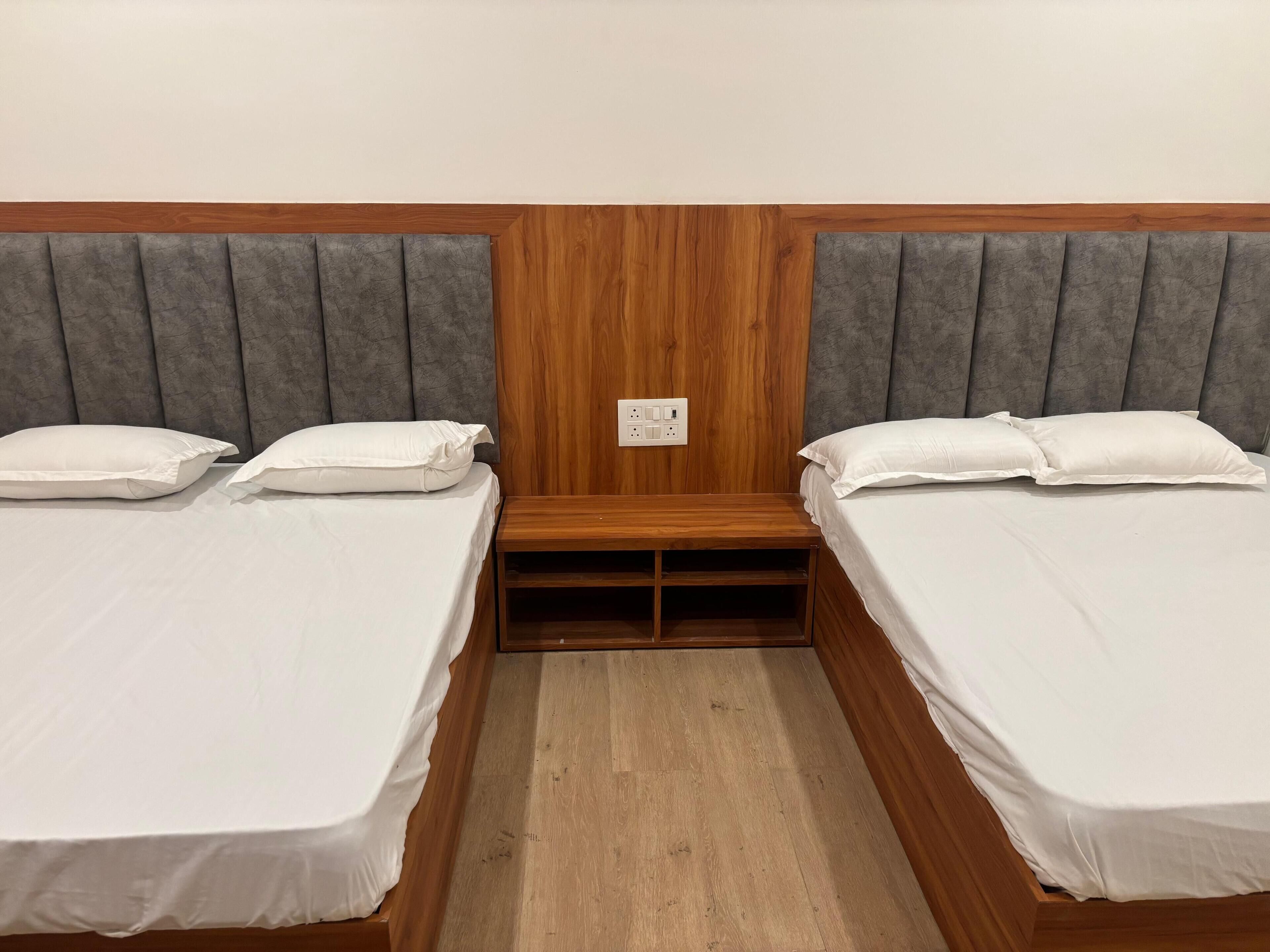 A room with two single beds, a wooden headboard, a small wooden nightstand, and a power outlet on the wall.