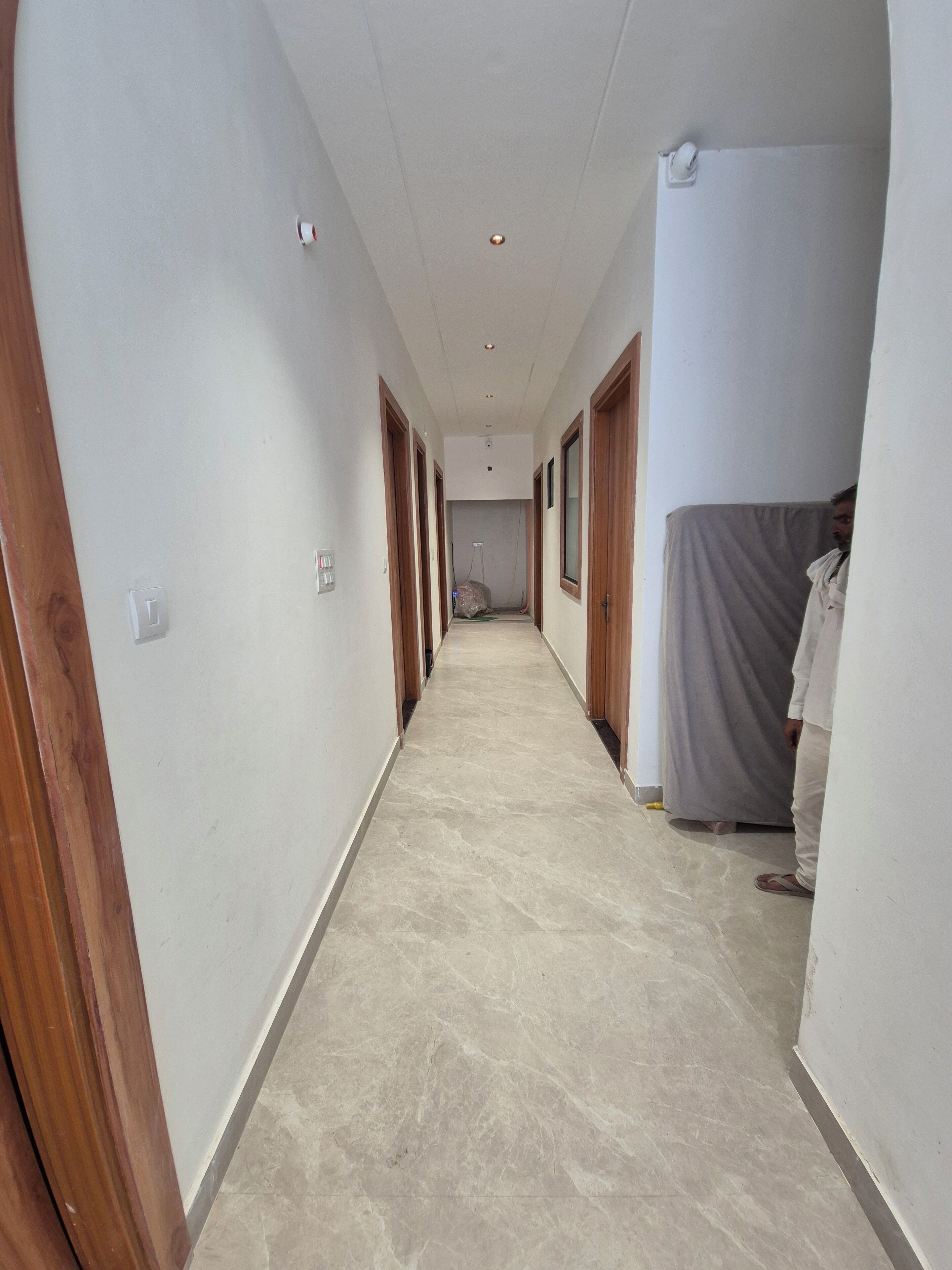 Un pasillo con puertas de madera, piso de baldosas y una persona al fondo.